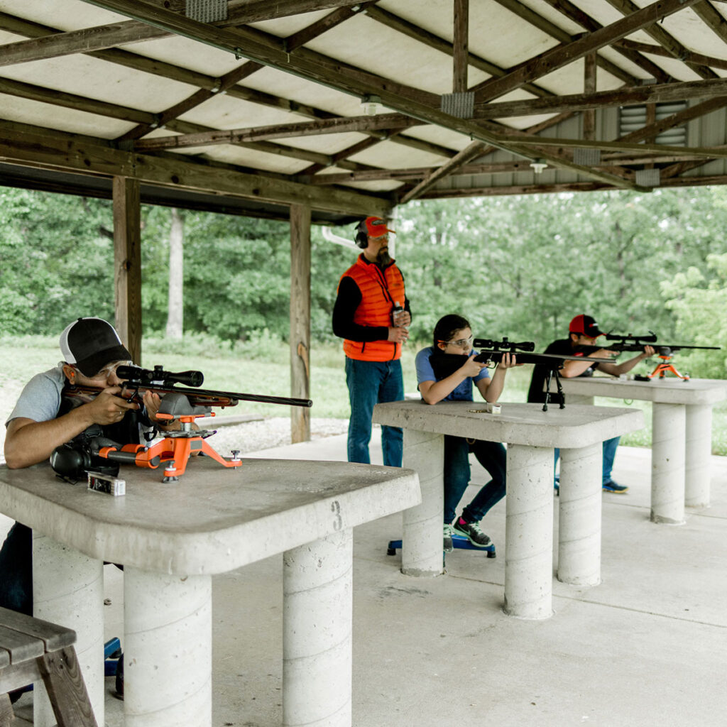 Three people aiming rifles under supervision of an instructor at a target range