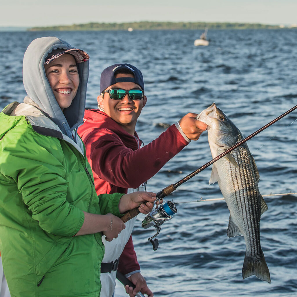 Two young adults on a boat with a striped bass