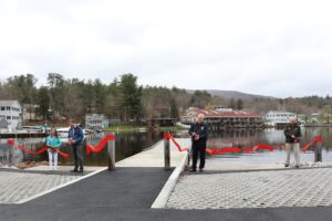 four adults cutting red ribbon in front of water