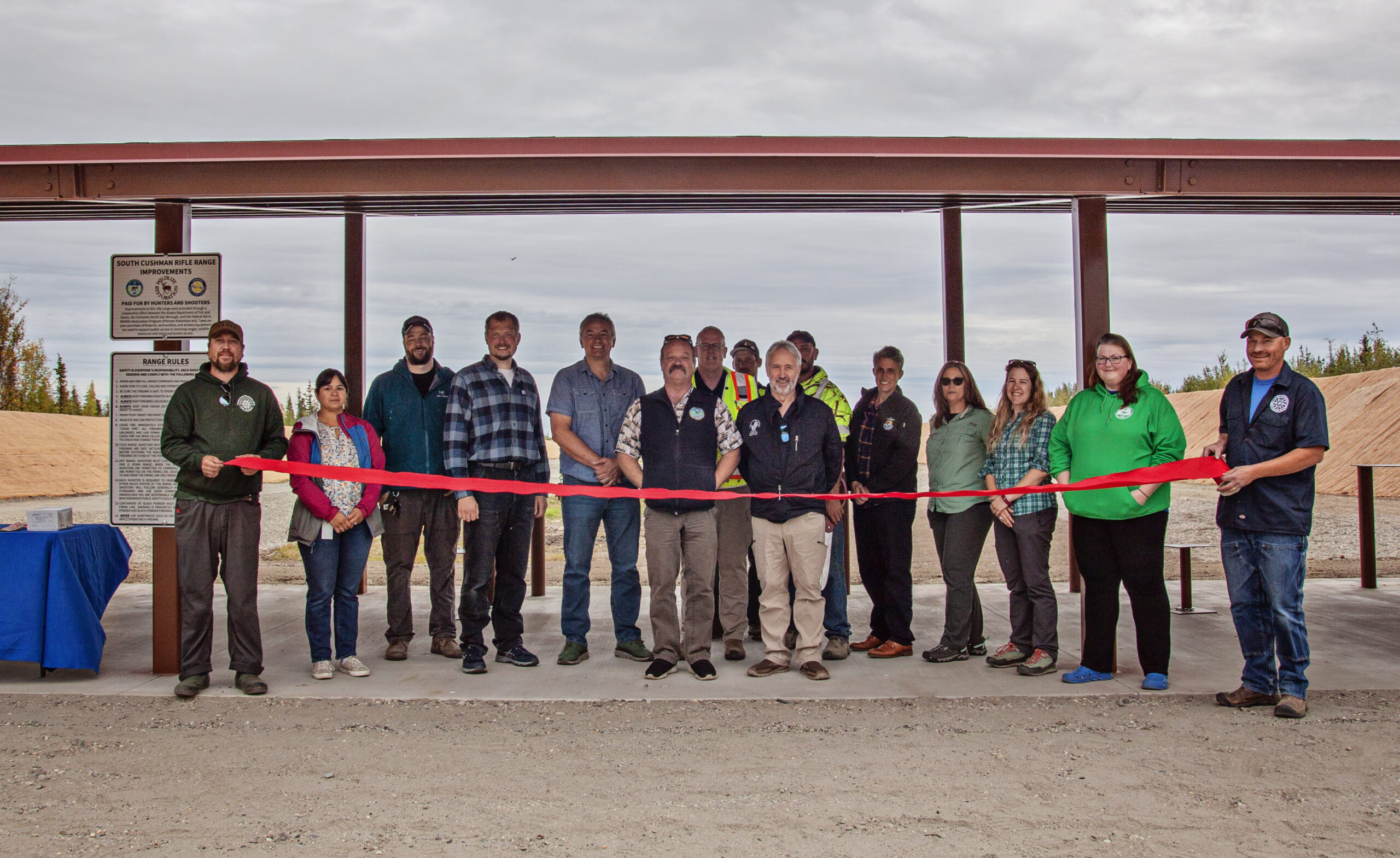 Group of adults standing behind a red ribbon at a shooting range