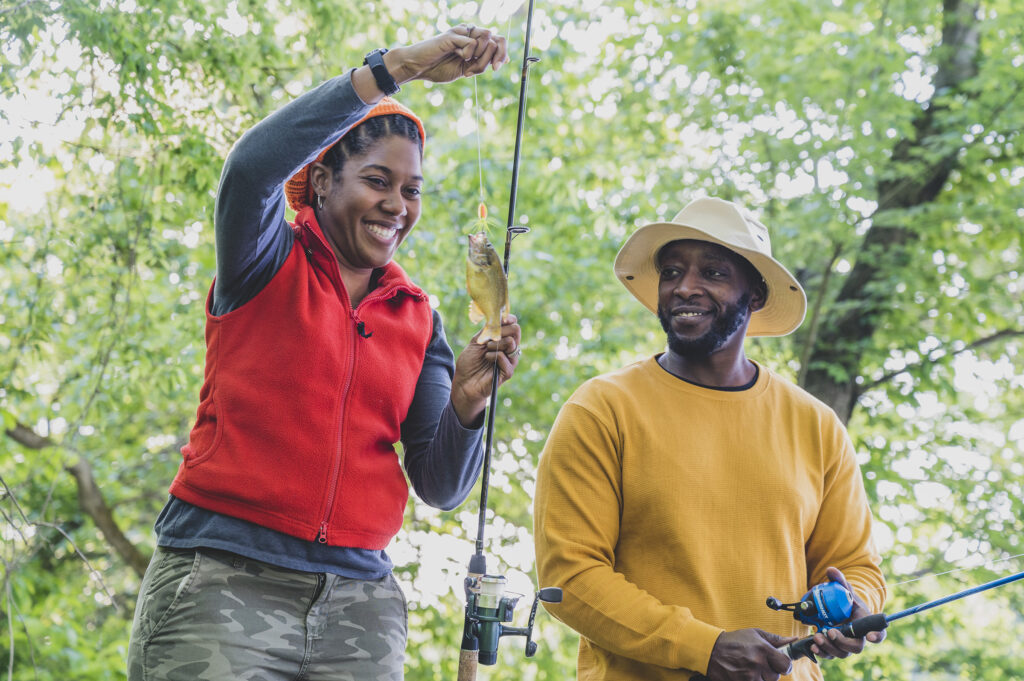 Man and woman smiling at small fish they just caught on their fishing rod.