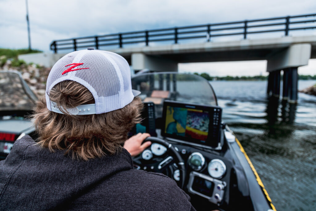 Young man pilots a boat under a road causeway while walleye fishing.