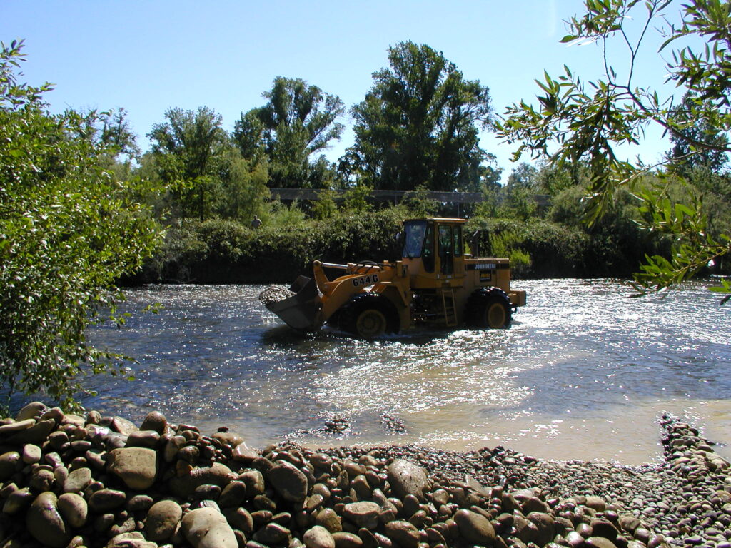 Loader in river water spreading gravel