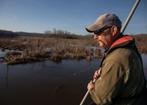 Biologist stands on bow of boat holding net to catch snakehead during survey.