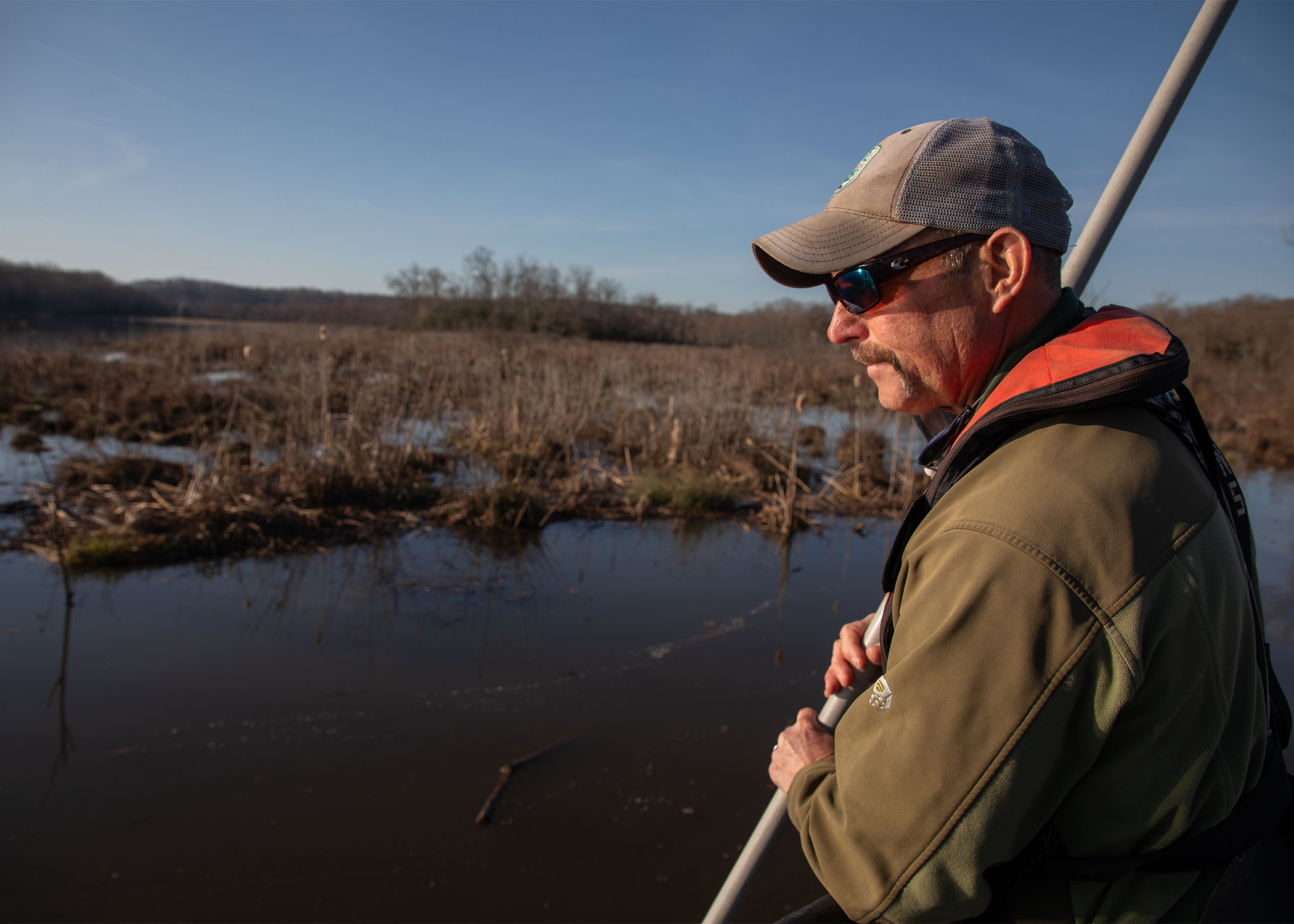 Biologist stands on bow of boat holding net to catch snakehead during survey.