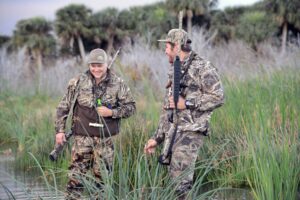 Two waterfowl hunters wade through wetlands.